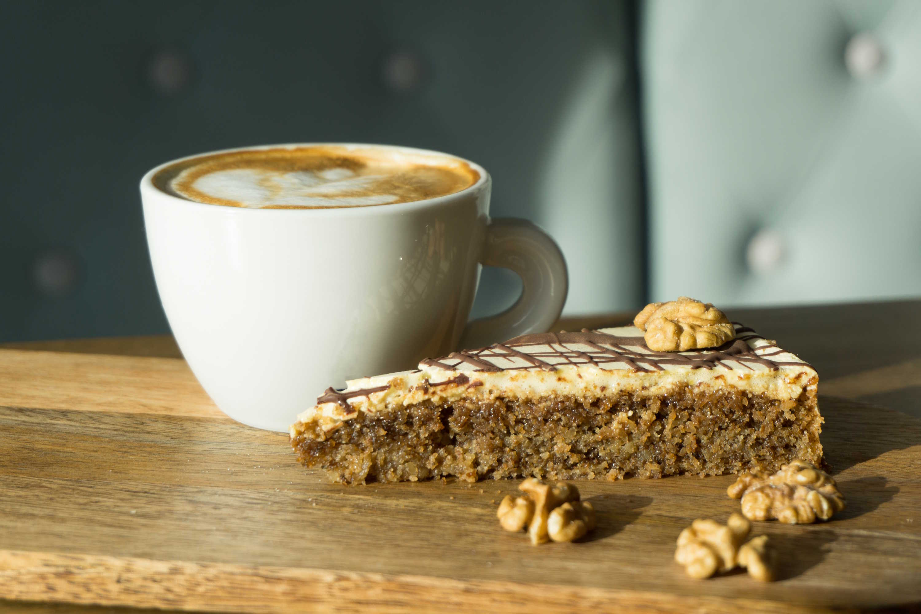 close-up shot of a cup of cappuccino next to a piece of cake with walnuts