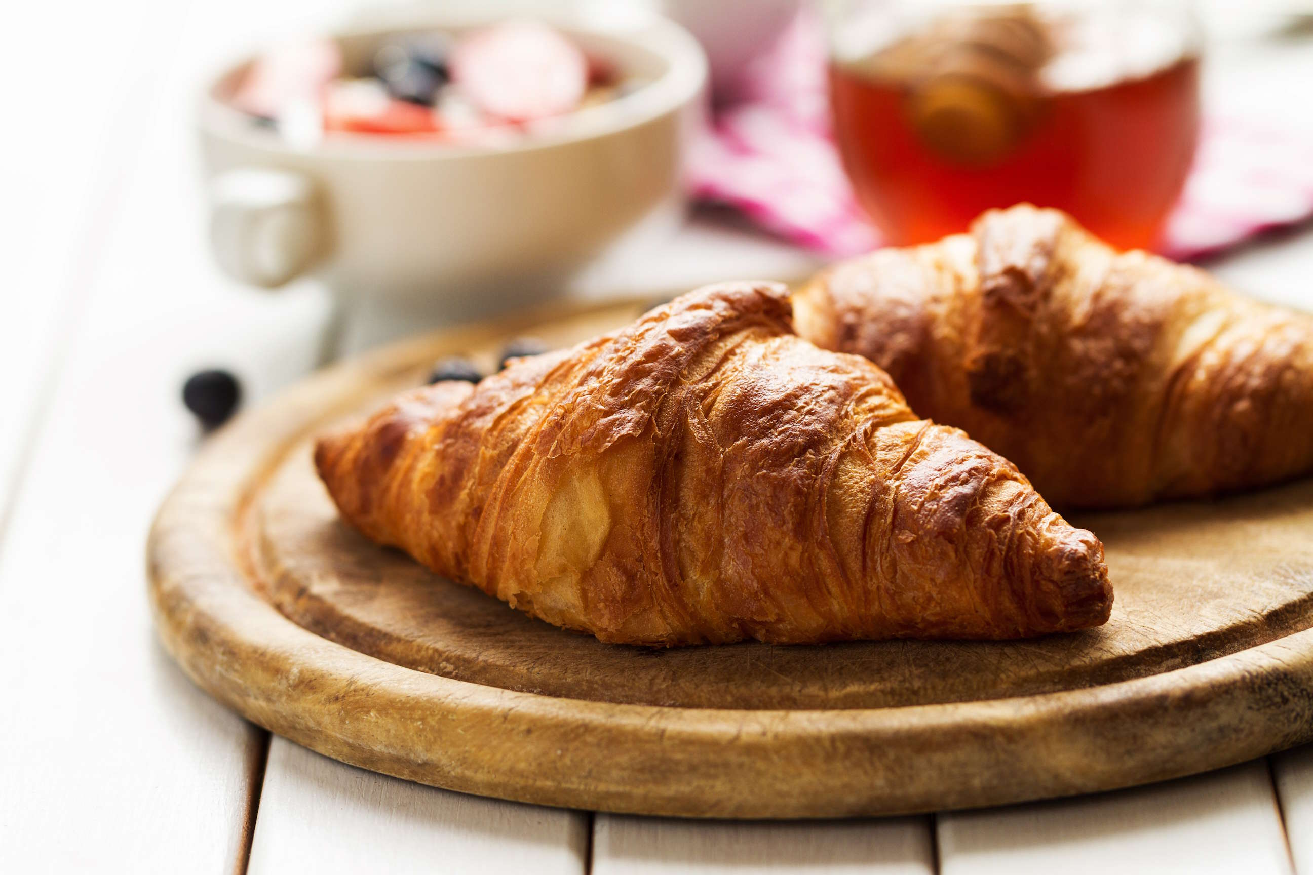 close-up shot of two croissants on a wooden board with a blurry background showing a bowl of granola and a glass of honey